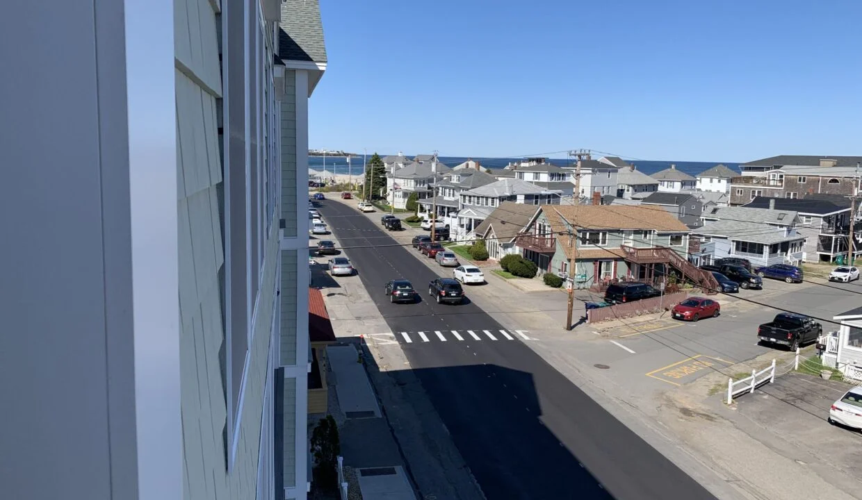 a view of a street with houses and a body of water in the distance.