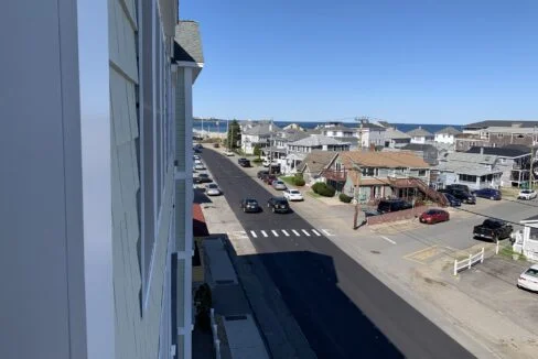 a view of a street with houses and a body of water in the distance.