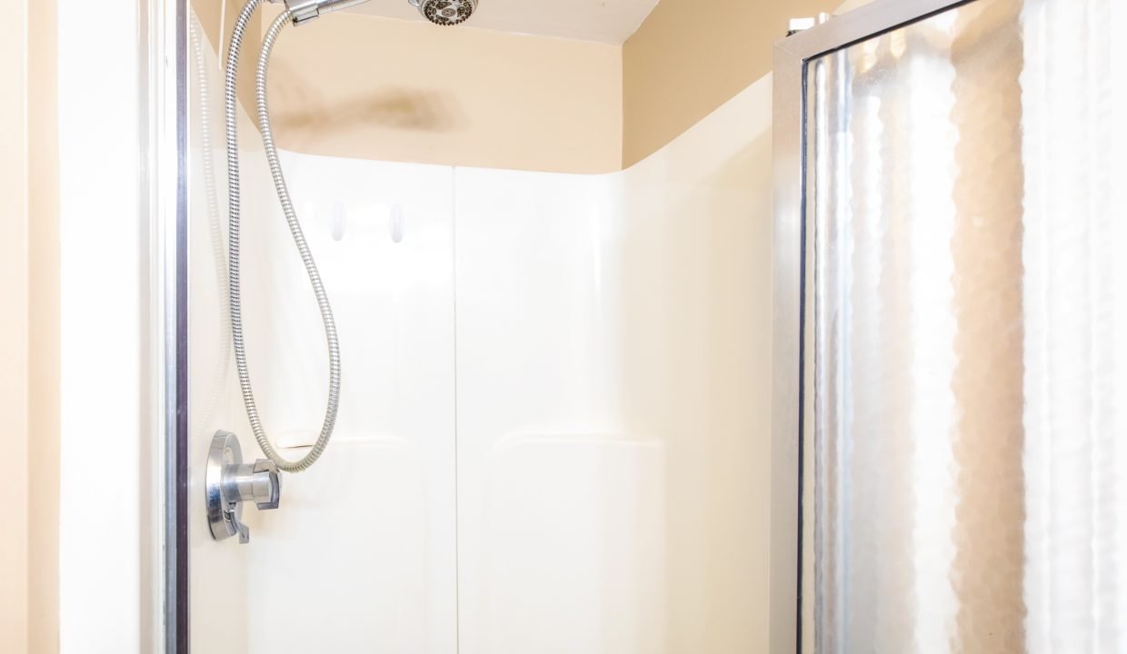 A shower with a flexible shower head, an off-white surround, and a partially visible frosted glass door.