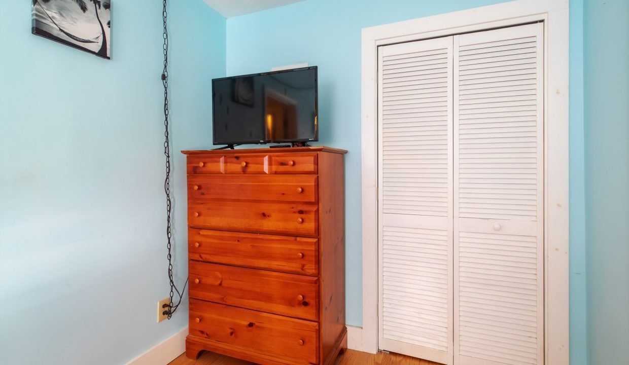 Room corner with a wooden dresser holding a flat-screen TV, blue walls, a louvered closet door, and a wall-mounted picture.