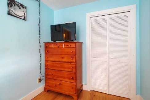 Room corner with a wooden dresser holding a flat-screen TV, blue walls, a louvered closet door, and a wall-mounted picture.