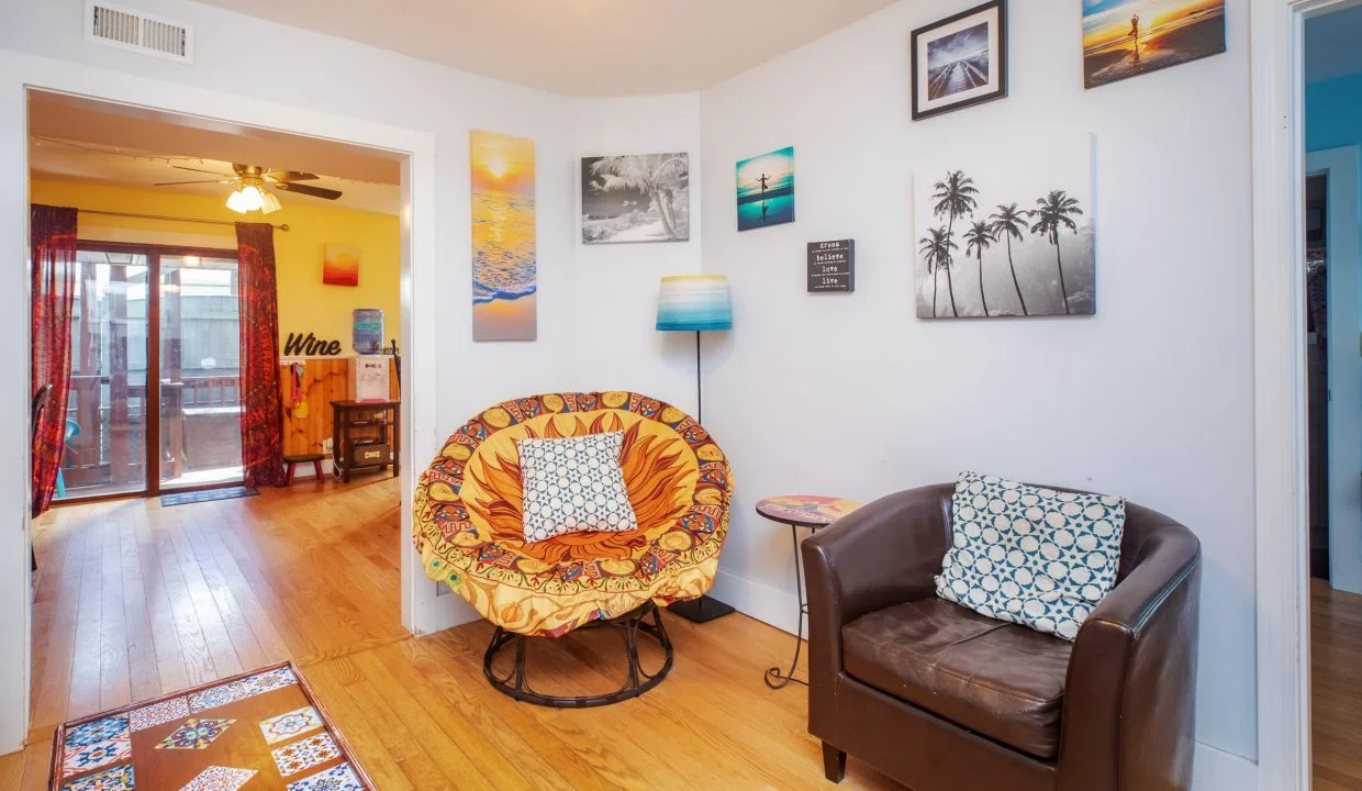 A small, cozy room with a brown leather chair and a circular chair with an orange cushion. The walls are decorated with various framed pictures. The room opens to a larger space with wooden floors.