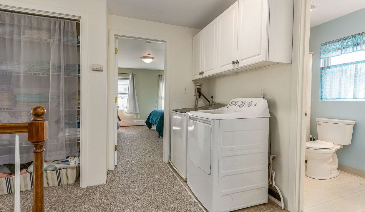 Hallway with a laundry area featuring a washer and dryer. To the left is a linen closet with a curtain, and a bedroom and bathroom are visible in the background.