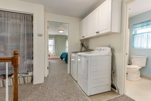 Hallway with a laundry area featuring a washer and dryer. To the left is a linen closet with a curtain, and a bedroom and bathroom are visible in the background.