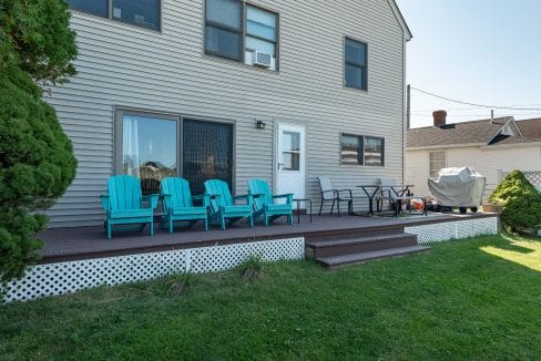 Backyard patio with turquoise Adirondack chairs, a table, and a covered grill. Steps lead to a grassy area.