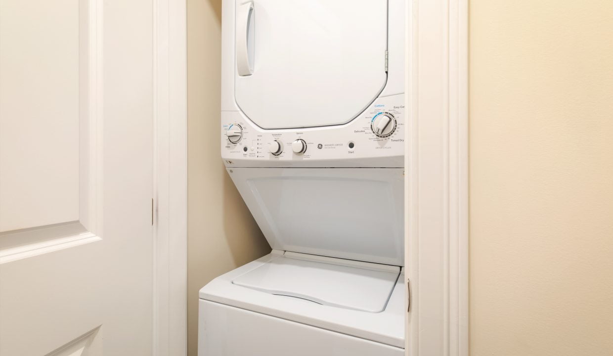 Compact laundry area with a white stacked washer and dryer set inside a narrow closet, with doors open to reveal the appliances.