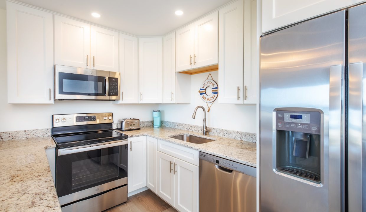 Modern kitchen with stainless steel appliances, including a refrigerator, oven, microwave, and dishwasher. White cabinets, granite countertops, and wood laminate flooring are also visible.