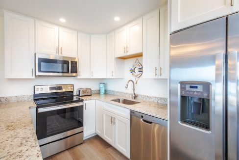 Modern kitchen with stainless steel appliances, including a refrigerator, oven, microwave, and dishwasher. White cabinets, granite countertops, and wood laminate flooring are also visible.