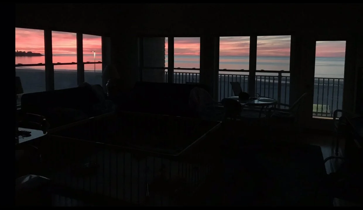 A living room with a view of the ocean and sunset.