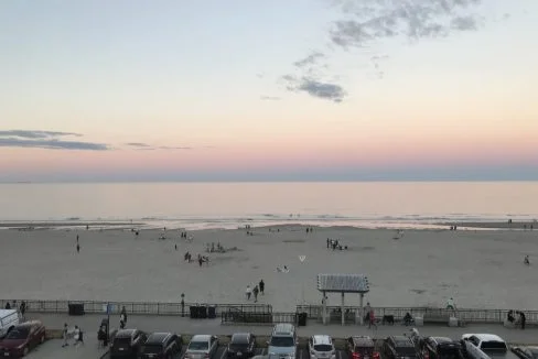 A view of the beach at dusk with cars parked in the parking lot.