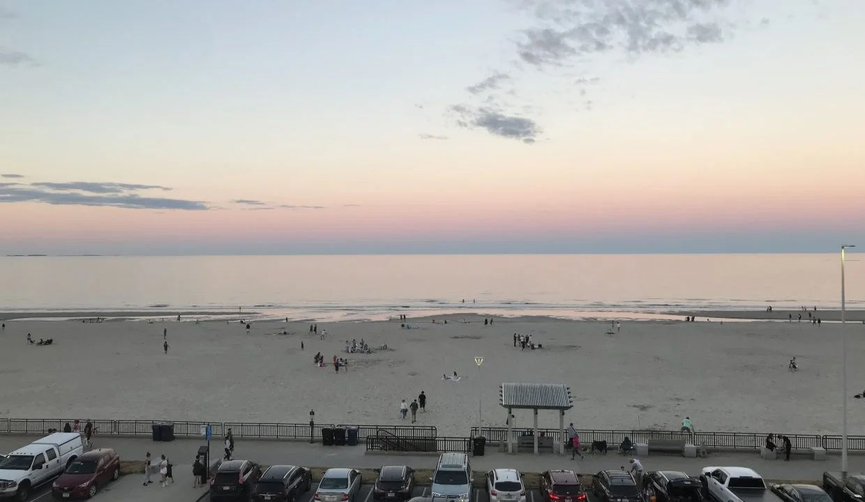 A view of the beach at dusk with cars parked in the parking lot.