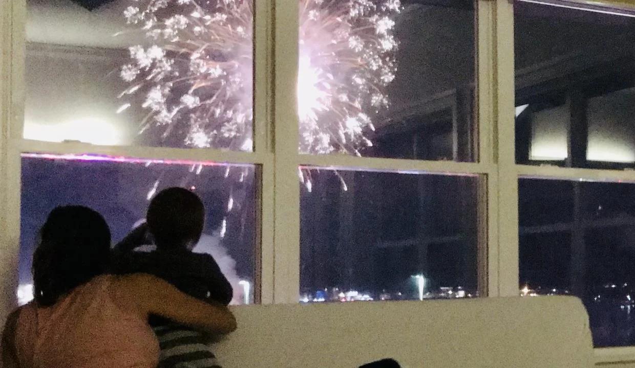 A woman and a child watching fireworks from a window.