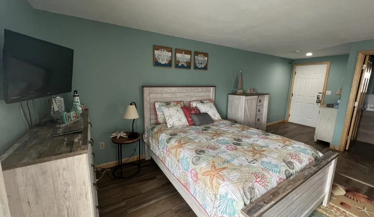 a bed room with a neatly made bed and a flat screen tv.