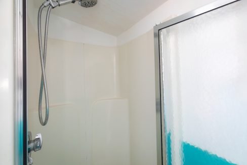 A small shower stall with a handheld showerhead, built-in white walls, and a glass door with a metal frame.