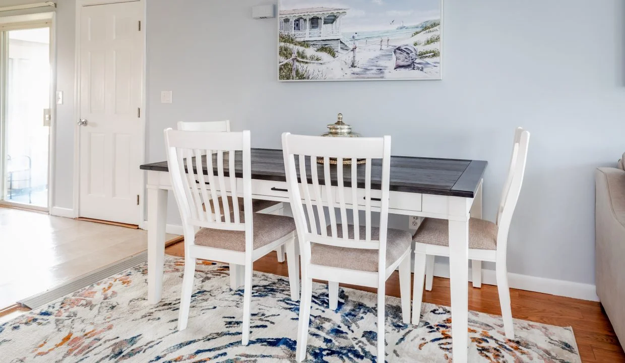 a dining room table with white chairs and a rug.