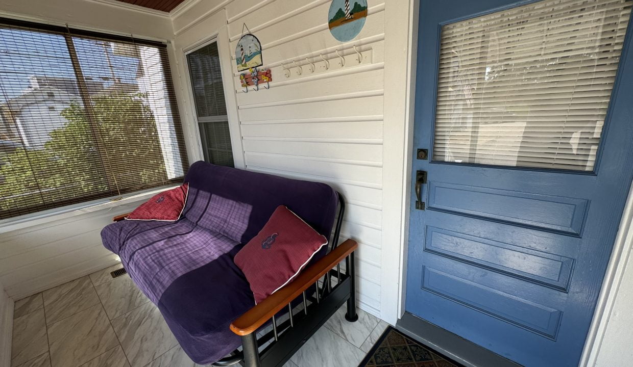 Enclosed porch with a blue door, a futon covered with a purple blanket, and decorative items on the wall. A window with closed blinds is on the left.