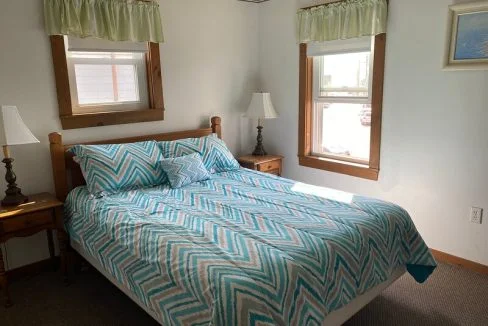 A neatly arranged bedroom with a patterned bedspread, two bedside tables with lamps, and a window with green valances.