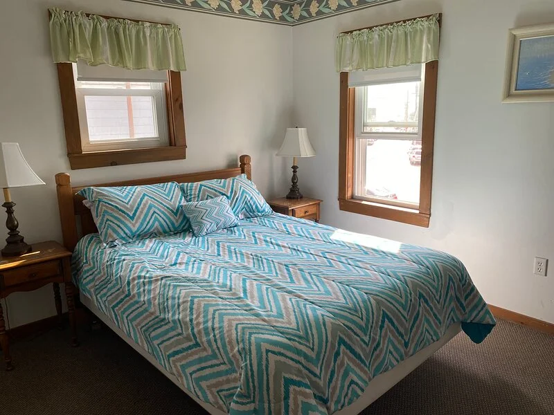 A neatly arranged bedroom with a patterned bedspread, two bedside tables with lamps, and a window with green valances.