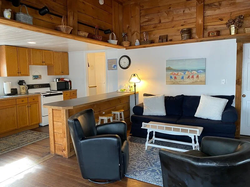 A cozy, wood-paneled living space with an open kitchen, couch, coffee table, and reclining chairs.