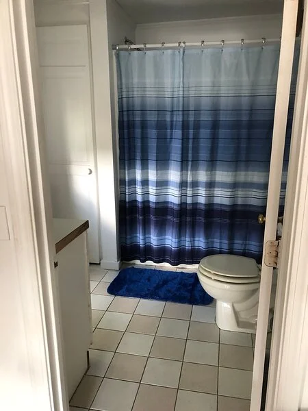 A small bathroom with a blue-striped shower curtain and coordinated blue bath mat.
