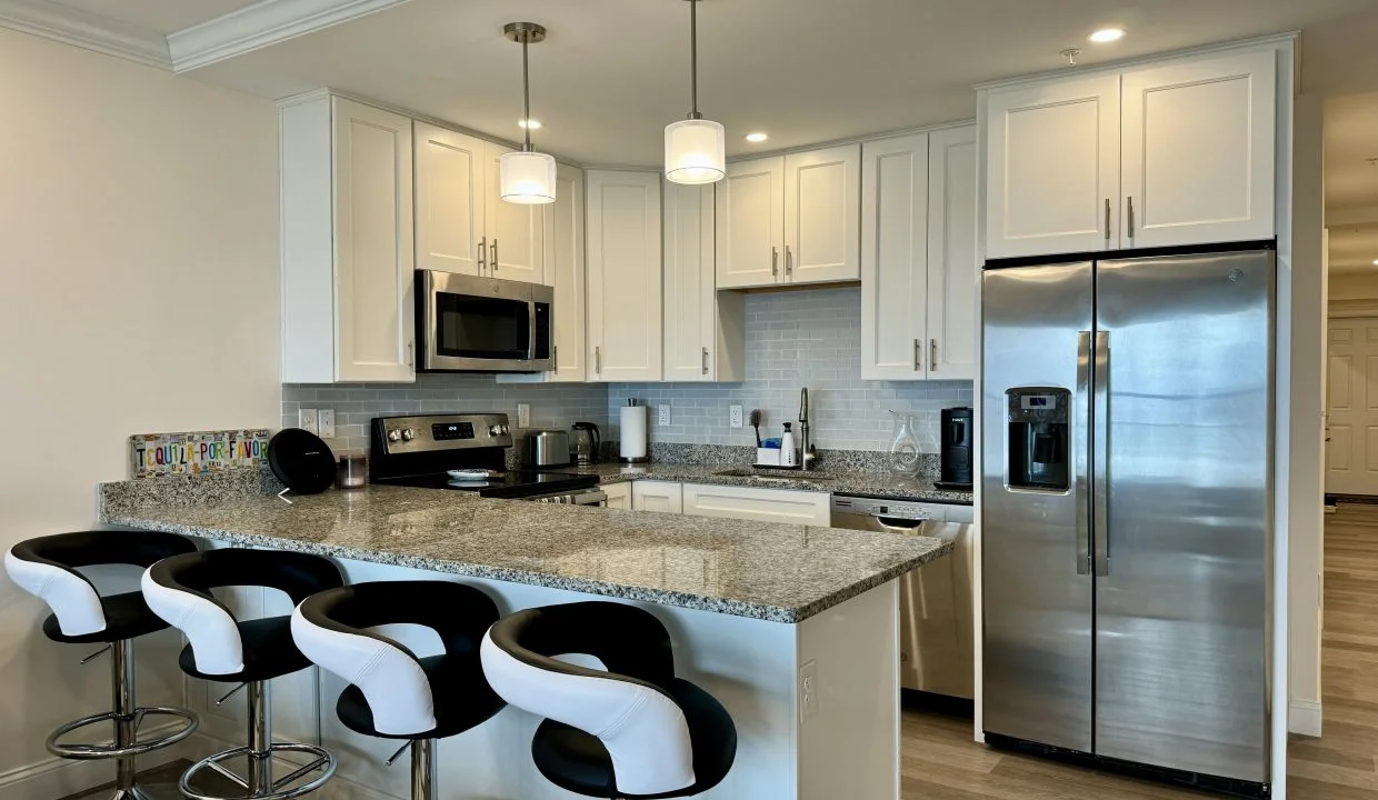 Modern kitchen interior with bar stools, stainless steel appliances, and white cabinetry.