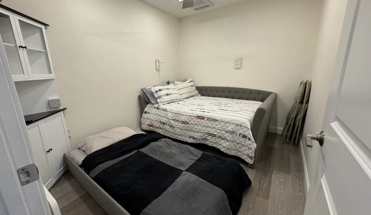 A small bedroom with a daybed, white cabinetry, and hardwood flooring.