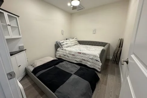 A small bedroom with a daybed, white cabinetry, and hardwood flooring.