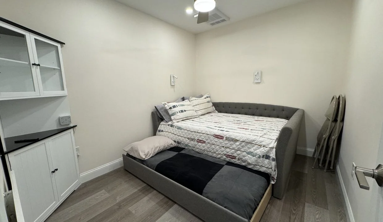 Modern minimalist bedroom with a gray upholstered bed, white built-in cabinets, and wood flooring.