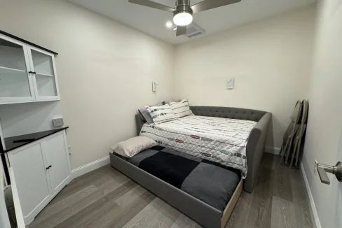 Modern minimalist bedroom with a gray upholstered bed, white built-in cabinets, and wood flooring.