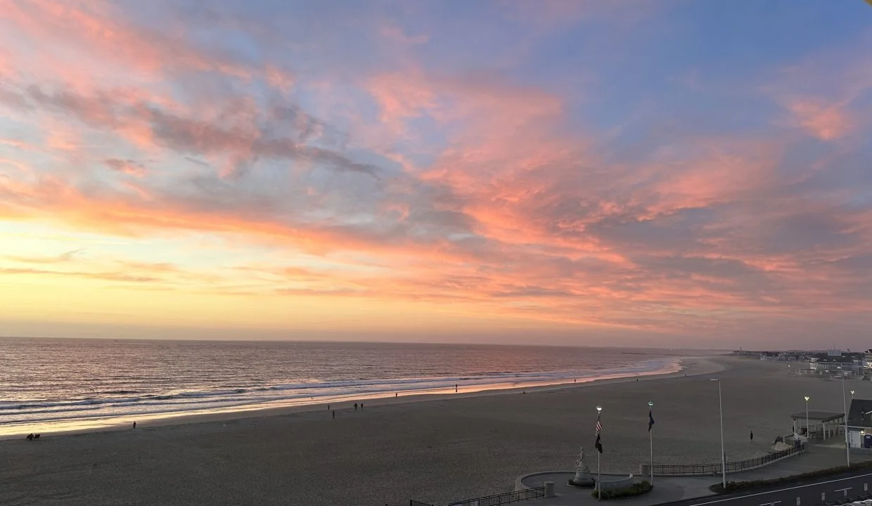 A coastal sunset with vivid pink and orange clouds over a tranquil beach and calm sea.