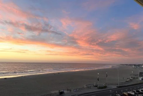 A coastal sunset with vivid pink and orange clouds over a tranquil beach and calm sea.