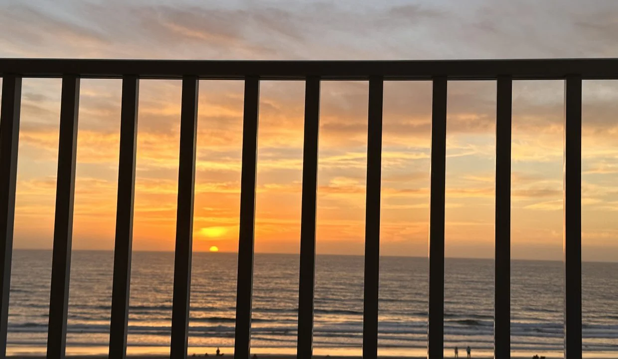 Sunset viewed through balcony railings overlooking the beach.