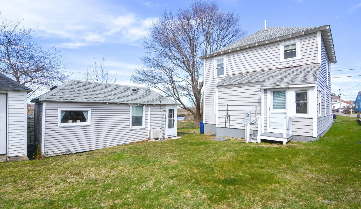 Two small, detached houses with white siding and gray roofs, situated on a grassy lot under a clear sky.