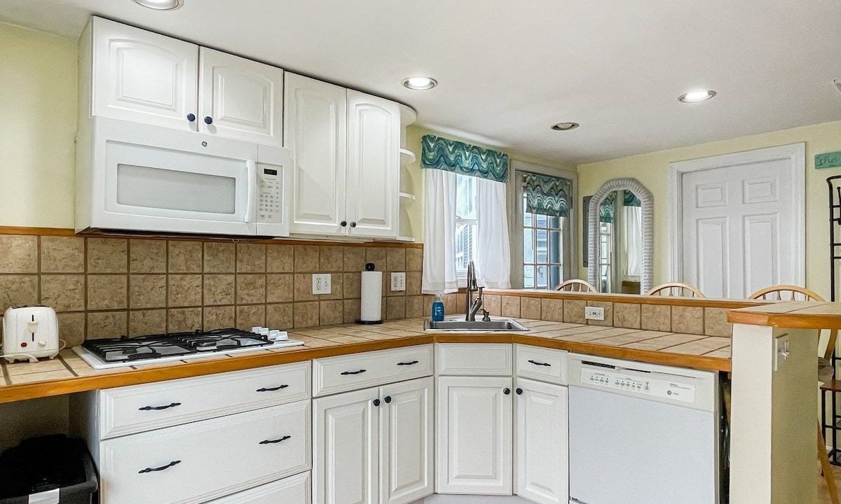 A bright kitchen with white cabinets, tiled backsplash, and built-in appliances, including a microwave and stove.