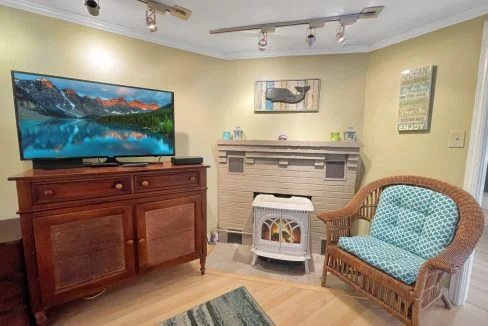 Cozy living room with a wicker chair, television on a wooden cabinet, fireplace, and decorative wall signs.