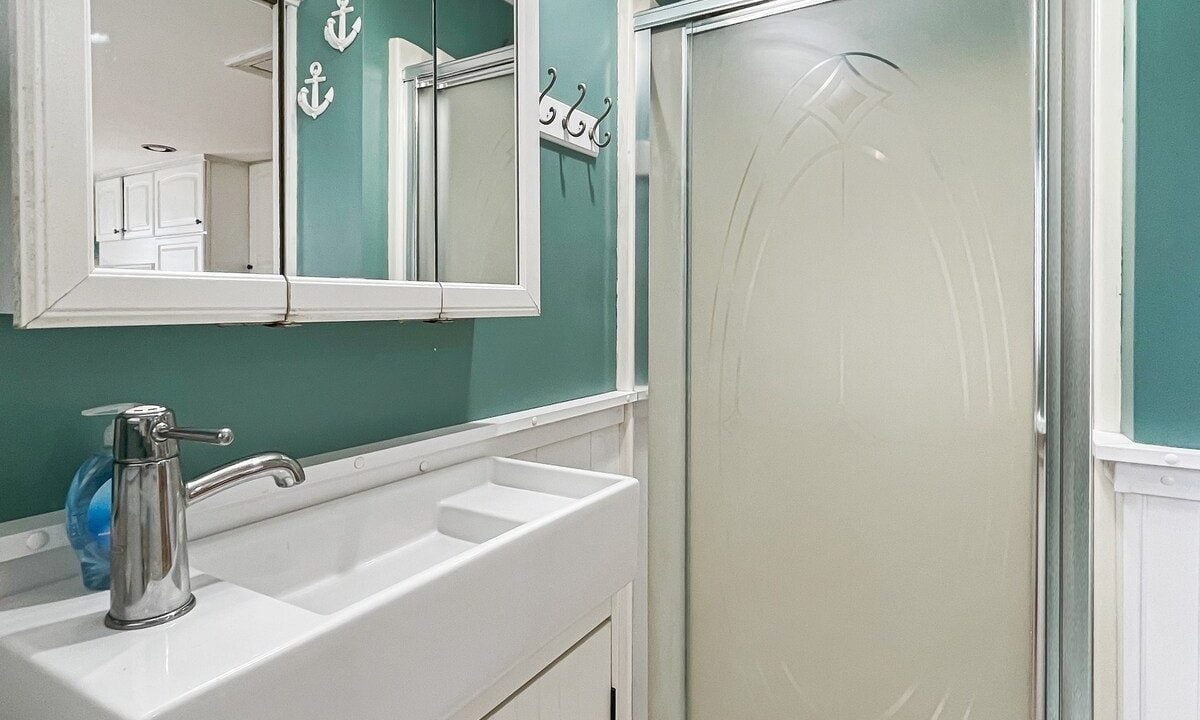 A nautical-themed bathroom featuring teal walls, white beadboard, and a standing shower with an anchor motif on the mirror.