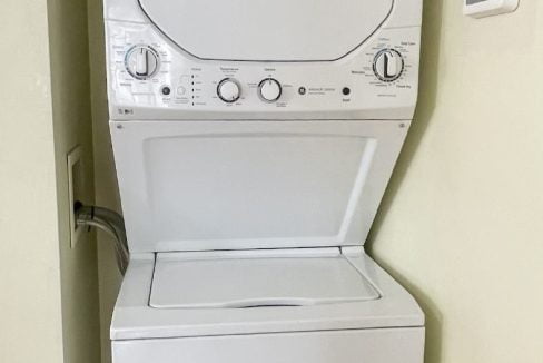 Stacked white washer and dryer in a narrow room, with control knobs and front loading doors visible.