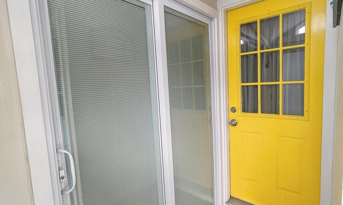 A small entryway with a bright yellow door and a white sliding screen door, featuring a 