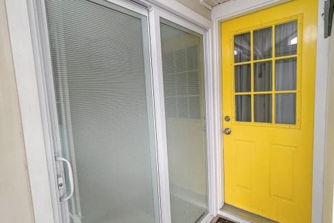 A small entryway with a bright yellow door and a white sliding screen door, featuring a 