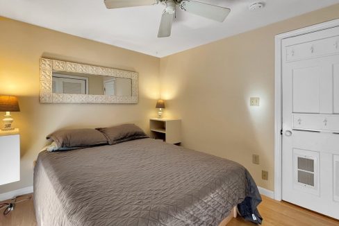 A neat bedroom featuring a large bed with gray bedding, twin nightstands with lamps, a ceiling fan above, and a closed door on the right.