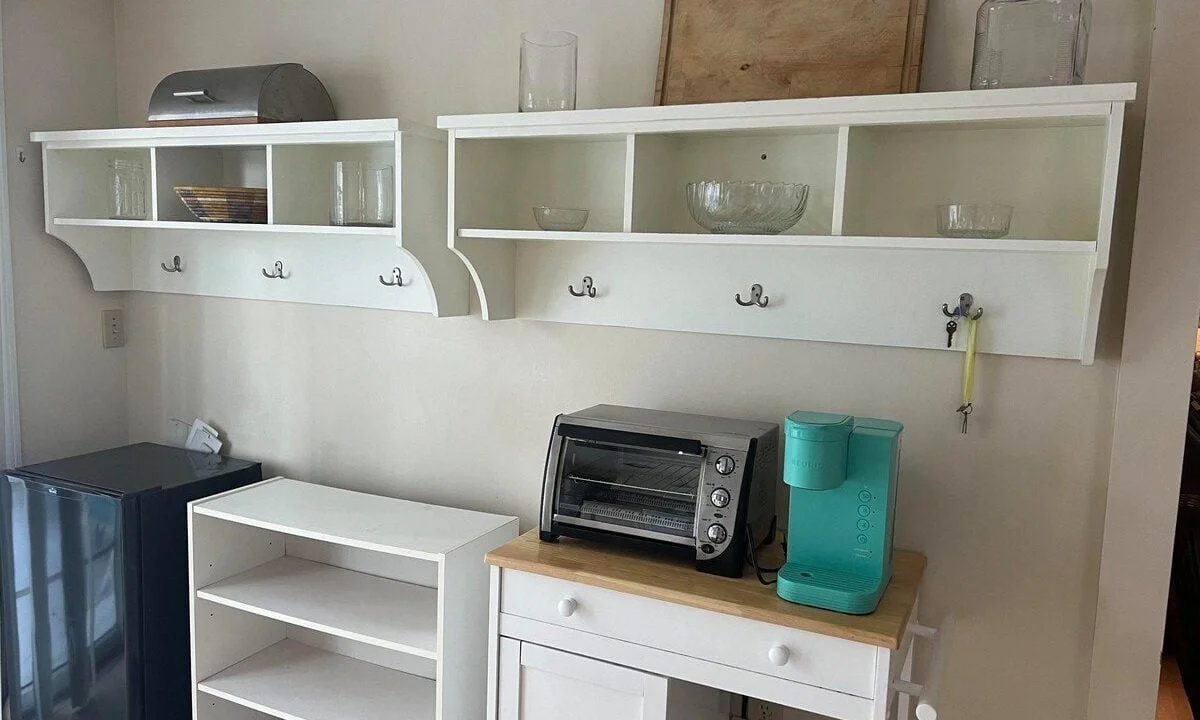 A small kitchenette with white shelves, a toaster oven, a mini-fridge, and various kitchen items.