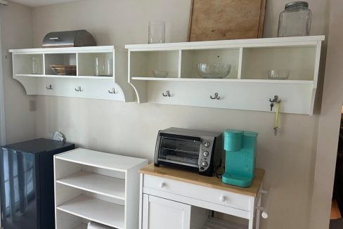 A small kitchenette with white shelves, a toaster oven, a mini-fridge, and various kitchen items.
