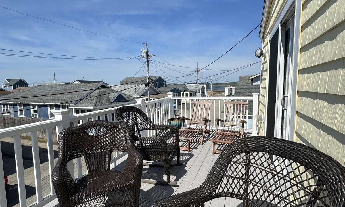 A rooftop deck with wicker chairs overlooks a neighborhood under a clear blue sky.