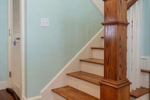 A small staircase with wooden steps and white railing, located next to a white door and framed pictures on a light blue wall.