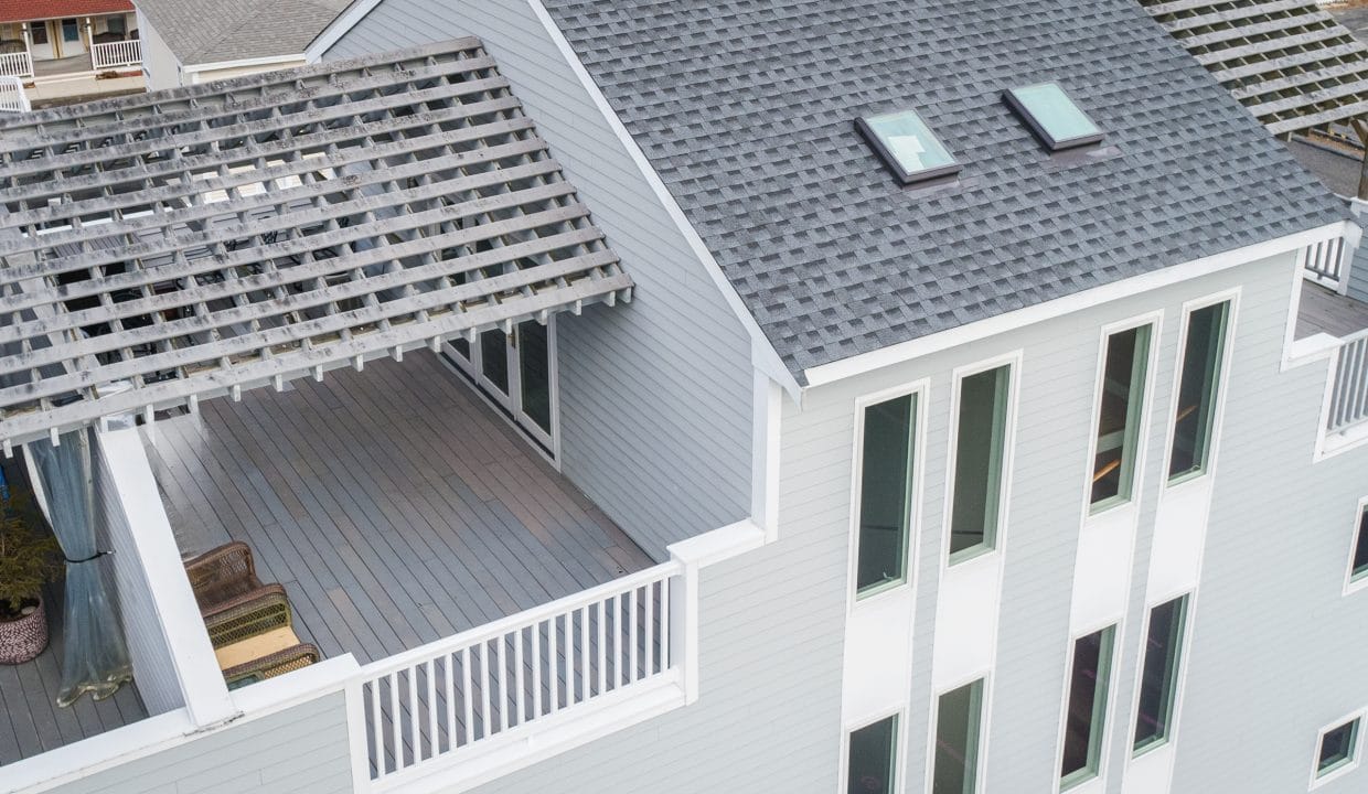 Aerial view of a modern gray house with a rooftop terrace featuring a wooden pergola and two skylights.