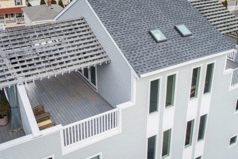 Aerial view of a modern gray house with a rooftop terrace featuring a wooden pergola and two skylights.