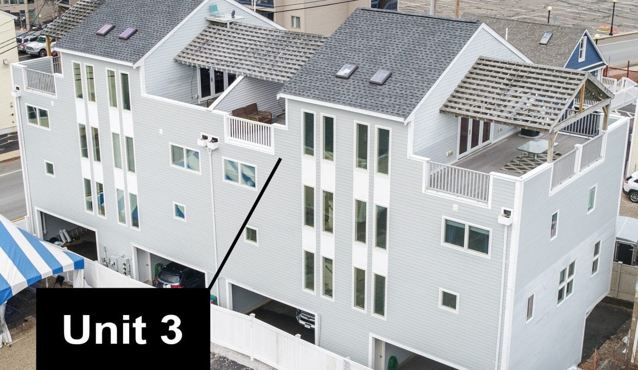 Aerial view of a row of three modern, pale gray townhouses with balconies. A black arrow points to the middle unit, labeled 