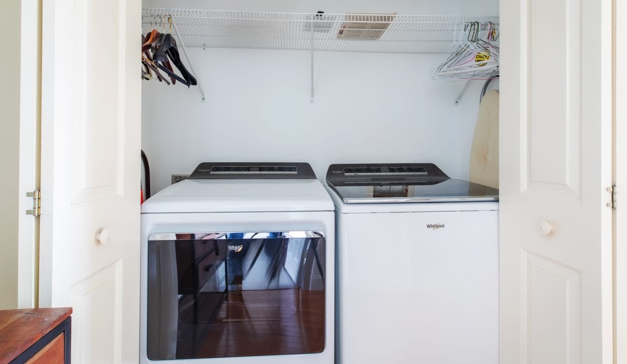 Laundry closet with white washing machine and dryer, shelf with hangers above, and an ironing board on the side.