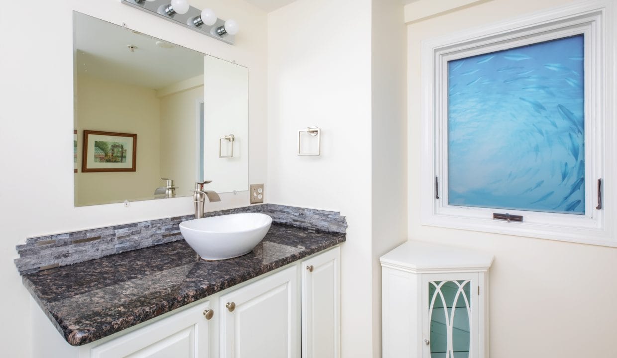 Bathroom with a white sink on a dark granite countertop, a wall-mounted mirror, and a window with an ocean-themed design.