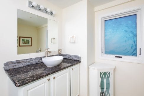 Bathroom with a white sink on a dark granite countertop, a wall-mounted mirror, and a window with an ocean-themed design.